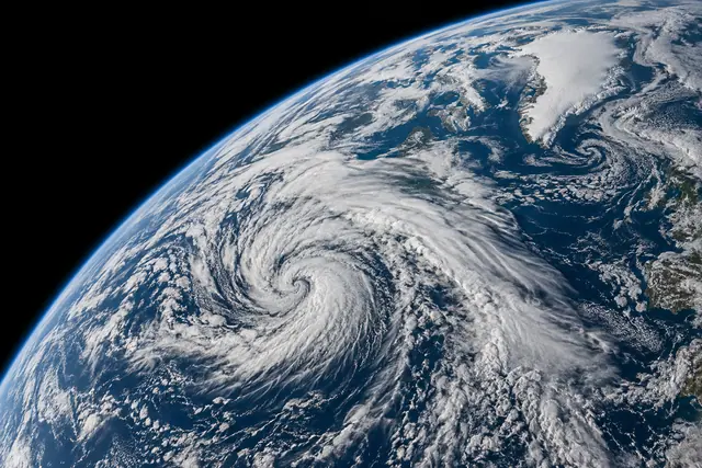 Terra vista do espaço com espiral de nuvens sobre o Atlântico, Groenlândia coberta de gelo e atmosfera azul.