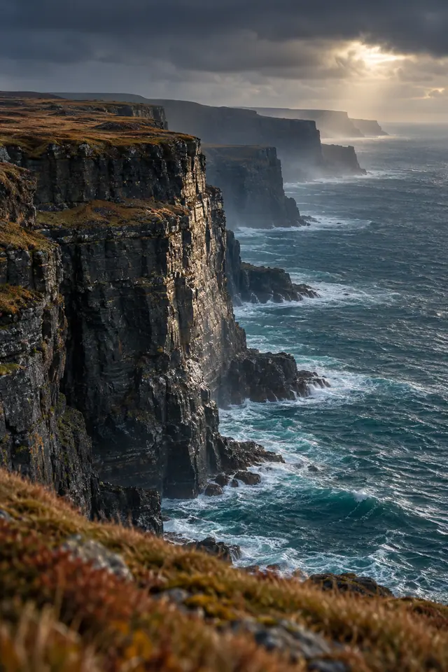Falésias escuras com vegetação outonal sobre o oceano, iluminadas por raios de sol entre nuvens densas.