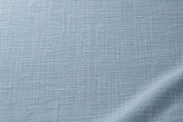 Textura de linho azul-claro com fios aparentes, luz suave e uma discreta dobra diagonal no canto inferior direito.