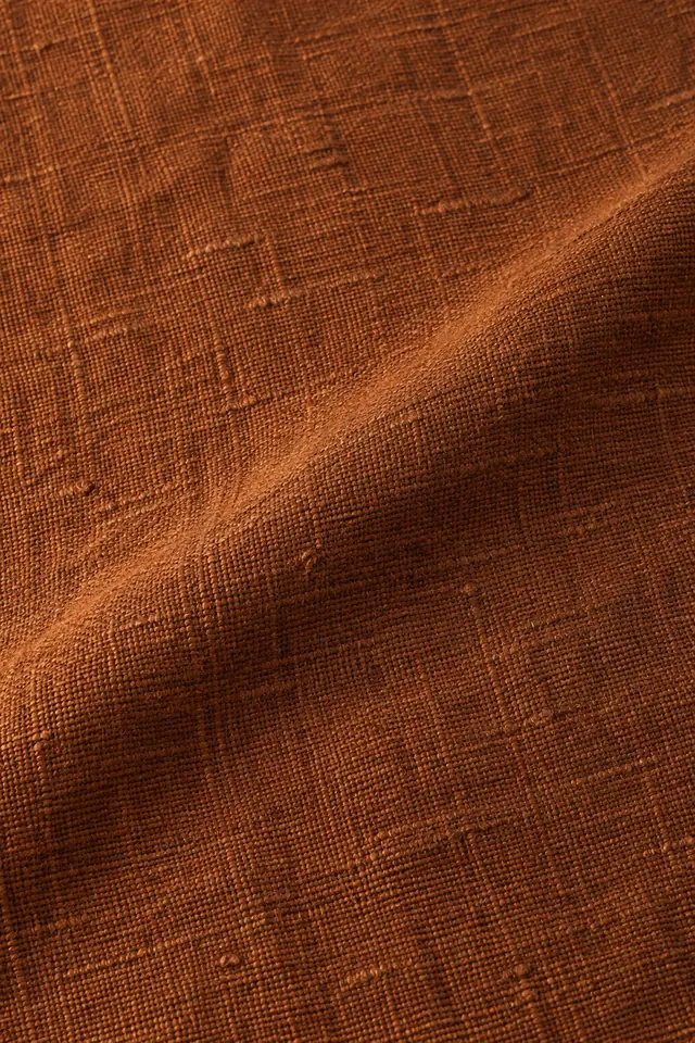 Textura de linho terracota com fios aparentes, dobra diagonal e luz quente lateral.