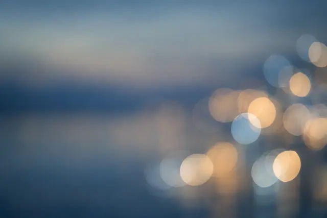 Fundo azul acinzentado com círculos de luz desfocados em dourado, marfim e azul concentrados à direita.