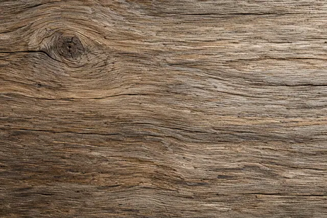 Textura de madeira envelhecida com veios horizontais, fissuras finas e um nó escuro no canto superior esquerdo.
