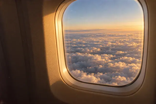 Janela de avião com vista para um mar de nuvens douradas no fim da tarde, em fotografia de estilo vintage.