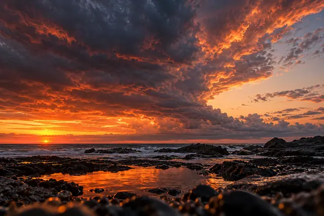 Nuvens escuras e alaranjadas ao pôr do sol sobre o mar e rochas, com reflexos dourados em uma poça.