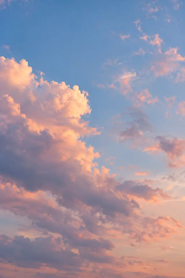 Nuvens em tons de pêssego, rosa e lilás sob um céu azul suave ao entardecer.