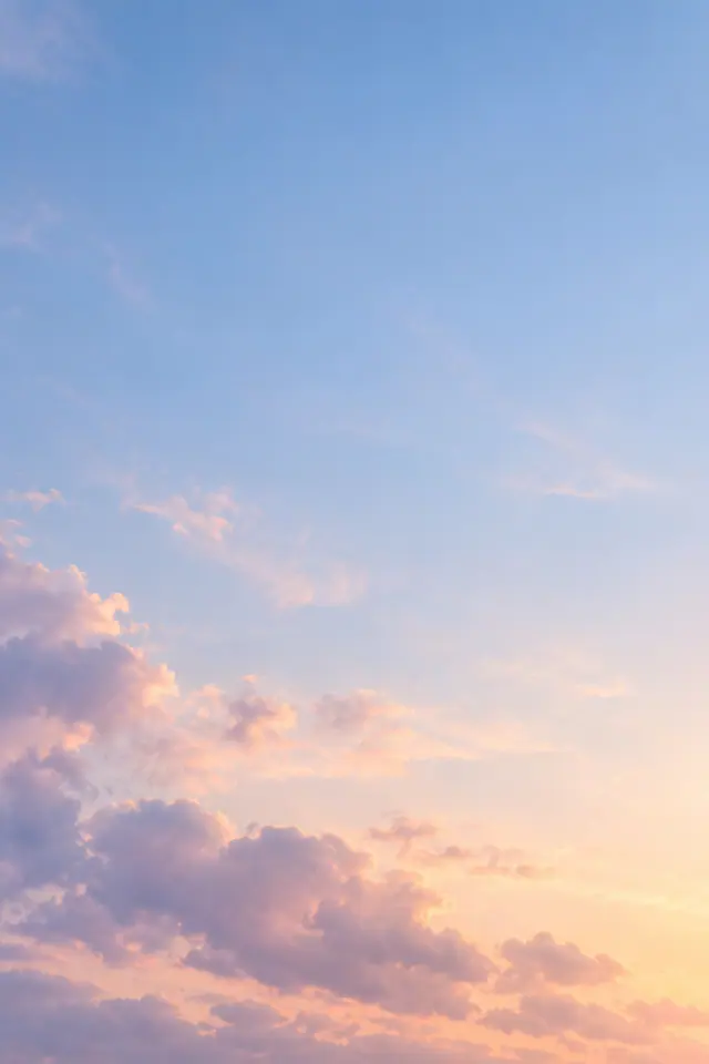 Nuvens rosadas e lilases iluminadas pelo amanhecer sob um amplo céu azul suave.
