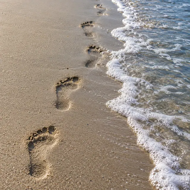 Pegadas de pés descalços na areia úmida ao lado de uma onda com espuma branca e água azulada.