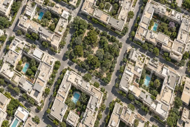 Vista aérea de quadras com prédios claros, piscinas e uma praça arborizada entre ruas em grade.