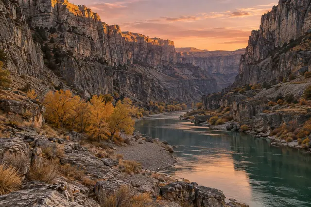 Rio verde entre paredões rochosos e árvores douradas, com reflexos do céu alaranjado ao pôr do sol.