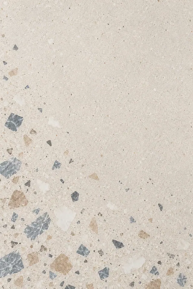 Terrazzo bege com fragmentos brancos e cinza-azulados concentrados à esquerda e na base, com ampla área livre.
