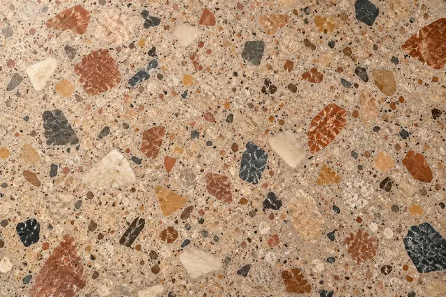 Textura de terrazzo bege com pedras irregulares em terracota, ocre, creme e carvão, vista de cima.